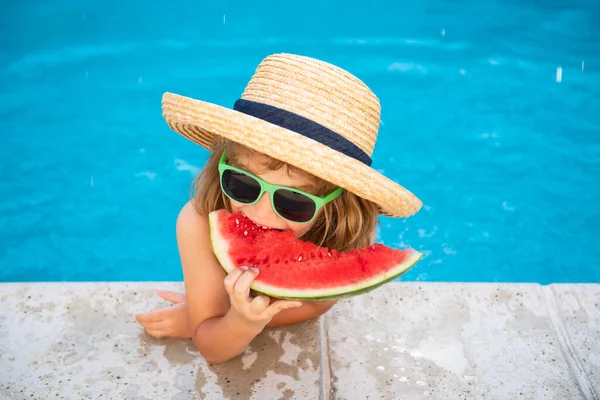 Niño comiendo sandía cerca de la piscina durante las vacaciones de verano. Los niños comen fruta al aire libre. Comida saludable para niños. Niño jugando en la piscina con una rebanada de sandía. — Foto de Stock