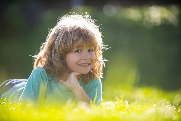 Porträtt av ett lyckligt skrattande barn som ligger på gräs i sommar naturpark. Närbild positiva barn ansikte. — Stockfoto