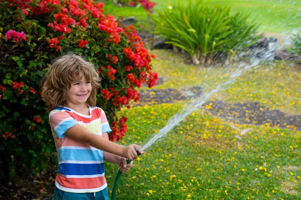 幸せな少年はホースから水を注ぐ。アメリカの子供時代。庭で子供の散水花。家庭菜園. — ストック写真