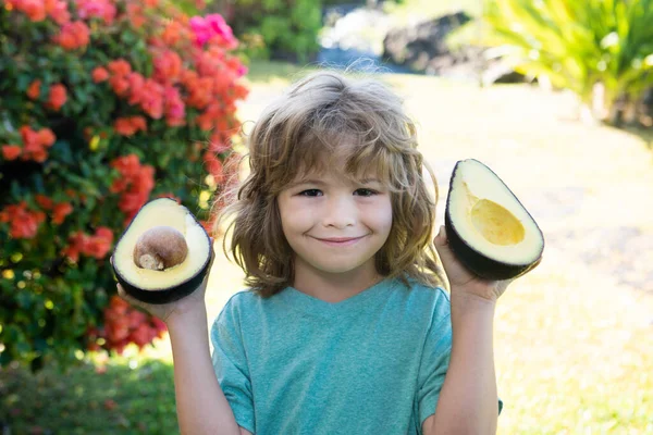 Närbild av barn med en halv avokado i handen, bredvid henne ligger en hel avokado. Friska barn koncept. — Stockfoto