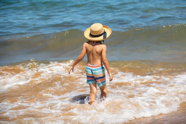 Vista posteriore del ragazzo sulle onde del mare. Gioca da spruzzi d'acqua del mare. Vacanze estive per bambini. — Foto Stock