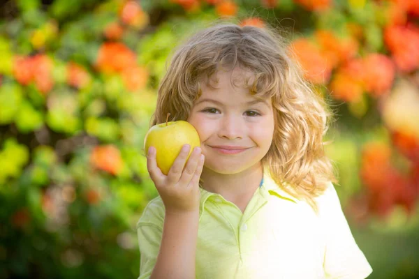 Портрет маленького мальчика, держащего и поедающего яблоко на зеленом фоне природы. — стоковое фото