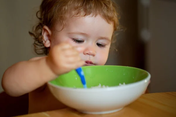 Portret uroczego białego dziecka z łyżką. Głodny bałagan dziecko z talerzem po zjedzeniu puree. — Zdjęcie stockowe