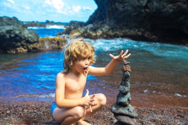Heyecanlı çocuk çakıl taşı plajında taş piramit yapıyor. İstikrarı, zen 'i, ahengi ve dengeyi simgeliyor..