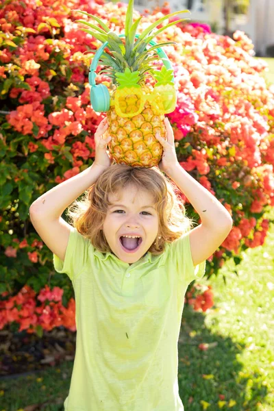 Little blonde kid hugging pineapple on nature background. Childhood, healthy nutrition, advertising. Close up kids funny face, copy space. — Stock Photo, Image