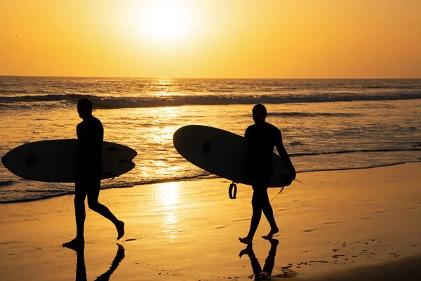 Silhouette de surfeurs portant leur planche de surf sur la plage du coucher du soleil. — Photo