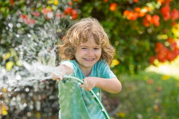 Счастливый мальчик наливает воду из шланга. Дети поливают цветы в саду. Садоводство. — стоковое фото