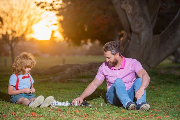 O pai joga xadrez com o filho. Pessoas ativas se divertindo e jogando xadrez no parque, passar o tempo com a criança. Família jogo fora. — Fotografia de Stock