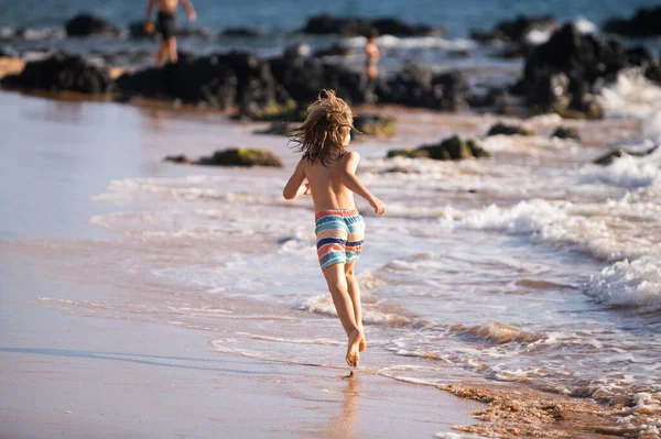 Vista trasera del niño saltando y corriendo en la playa del mar. — Foto de Stock