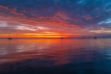 Gökyüzünde gün batımı ve renkli bulutlar. Güneşin doğuşuyla sakin deniz.