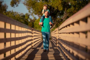 Baba, yaz parkı geçmişine rağmen oğlunu sırtında taşıyor. Baba ve Oğul yaz parkında eğleniyor..