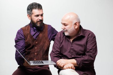 Yetişkin eğitimi. Babasıyla mutlu genç adam dizüstü bilgisayarda komik videolar izlerken eğleniyor. Yaşlı baba ve yetişkin oğul internette internet kullanırken gülümsüyor..