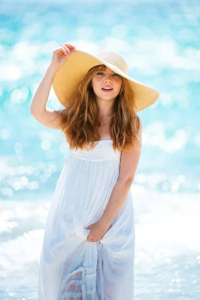 Belle fille avec chapeau de paille profitant du bain de soleil à la plage. Jeune femme bronzée profitant de la brise au bord de la mer. Femme insouciante souriant avec océan de mer en arrière-plan. — Photo