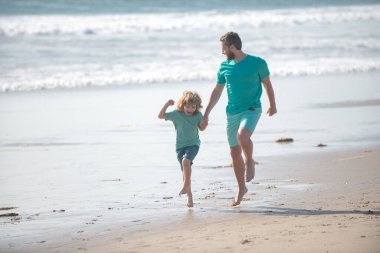 Mutlu aile kavramı. Baba ve oğul yaz plajında koşuyor. Baba ve çocuk dışarıda oynuyorlar..