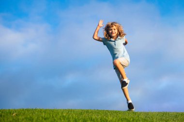 Little adorable boy running on grass. Excited kid play the green grass. The child has blond long hair and a t-shit. The concept of harmony with nature and care for ecology. Healthy lifestyle.