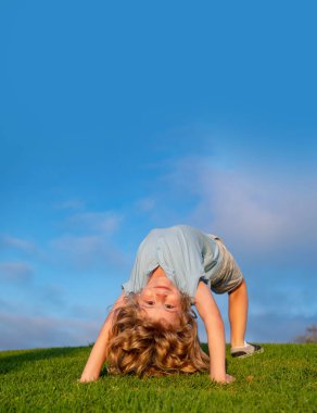 Mutlu çocuklar yaz parkında çimenlerde baş aşağı oynuyorlar. Çocuklar doğada spor yapar. Boşluğu mavi gökyüzünde kopyala.