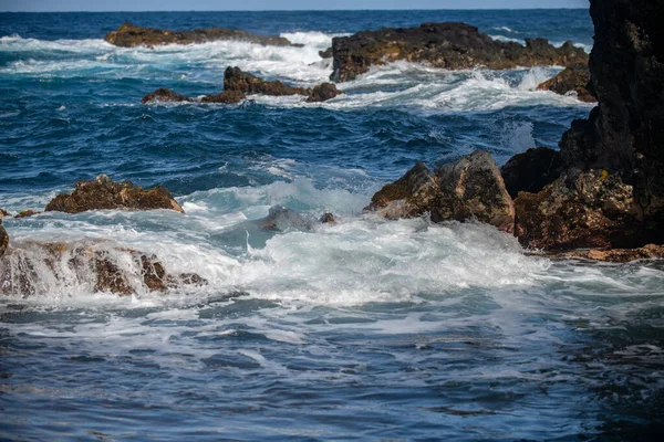 Gekoelde zwarte lava verslagen door de Atlantische Oceaan golven. Zicht op zee golven raken rotsen op het strand. Golven en rotsen. — Stockfoto