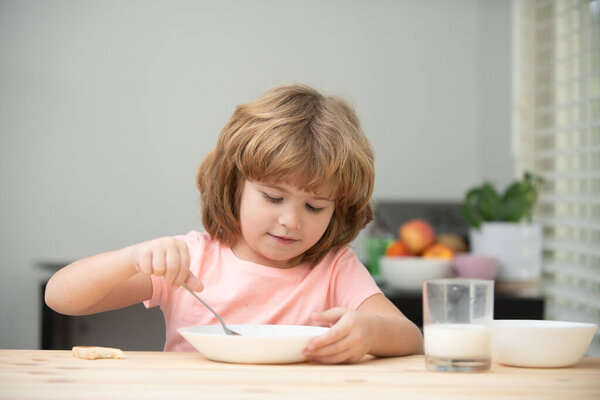 Белый мальчик-младенец ест здоровый суп на кухне. Крупный план милого маленького мальчика, поедающего вкусную кашу или крупы с молоком дома, сидящего за столом на кухне.