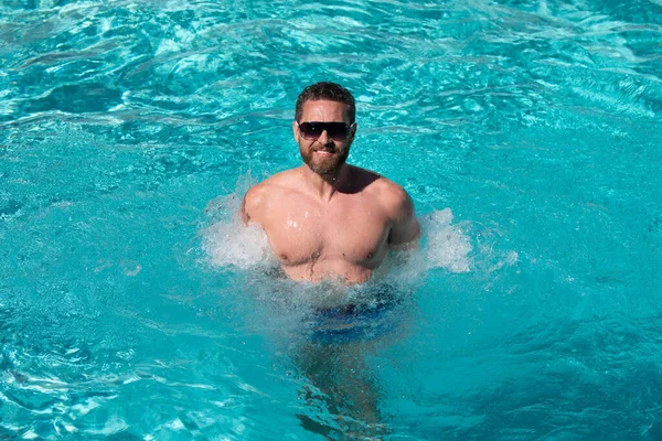 Handsome man in sunglasses swimming in pool. Summer resort. Summertime vacation. — Stock Photo, Image