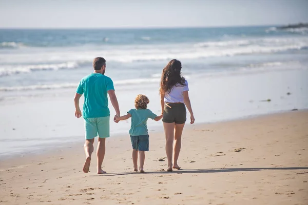 Vista posteriore della famiglia felice sulla spiaggia. Persone che si divertono durante le vacanze estive. Padre, madre e figlio che si tengono per mano contro il mare blu. Vacanza concetto di viaggio. — Foto Stock