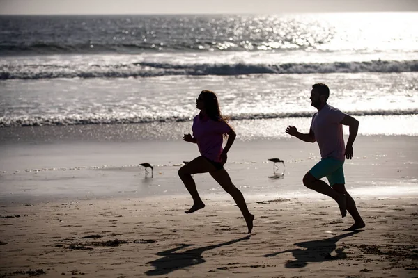 Couple courant sur la plage. Silhouette de jeune homme et de jeune femme courant le long de la mer. — Photo