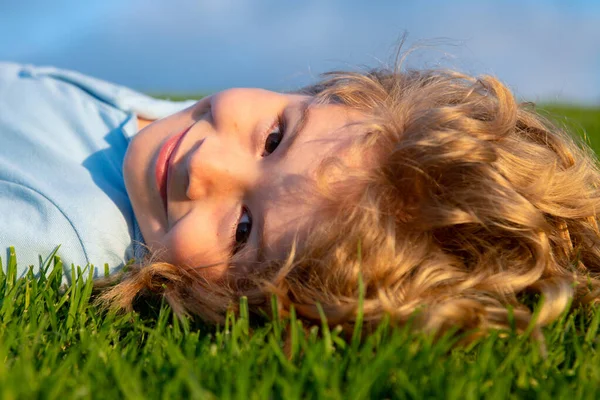 Tråkigt barn som ligger på den gröna sommarängen på sommaren på naturen. Glad unge kul med glada leende ansikte. Omsorgsfritt barn. — Stockfoto