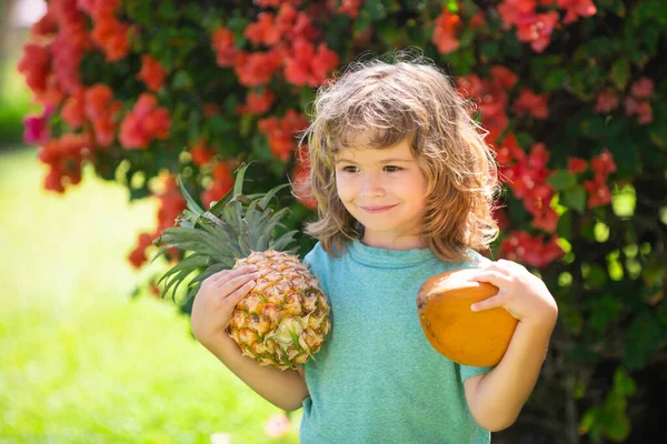 Niño sosteniendo piña y coco sonriendo con cara feliz en el patio. Frutas de verano. — Foto de Stock