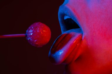 Close up lips with lollipop isolated, sexy blowjob, sensual mouth with lipstick eats sweets. Sexy design for women and girls. Beauty lips on neon lights. Night club background.