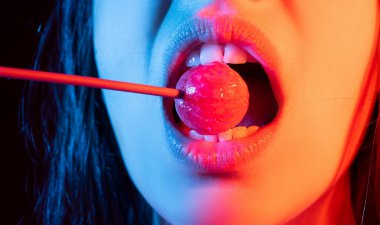 Cazibeli ağız kırmızı dudaklı lezzetli lolipopları yalıyor. Lolipop berbat. Seksi kadın dudağı. Lolipopu olan şehvetli, kırmızı dudaklı bir kadın. Neon ışıklar üzerine çikolata konsepti.