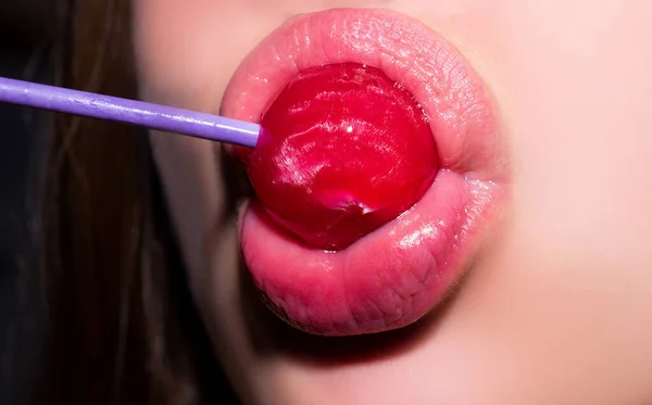 Sání rtů. Detailní ženské rty s růžovým leskem na rty drží v ústech červené lízátko cukroví. Lízátko na tváři. — Stock fotografie