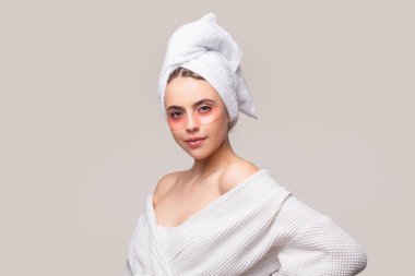 Göz bandı takan bir kadın. Kafasında havluyla portre kızı yakın plan. Göz maskeli kozmetik bantlar. Kadın yakından bakıyor. Gözlerinin altına göz bandı yapıştıran, gözlerinin etrafındaki hassas ciltle ilgilenen bir kadın..