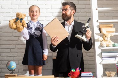 Öğretmen ilkokul derslerinde öğrenci bir kıza yardım ediyor. Öğrenci kız, öğretmenle aynı sınıfta okuyor..