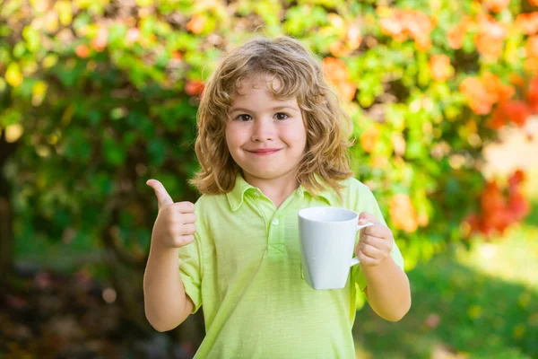 İyimser beyaz çocuk su içiyor, elinde bardağı tutuyor ve yeşil arka planda izole bir şekilde gülümsüyor.. — Stok fotoğraf