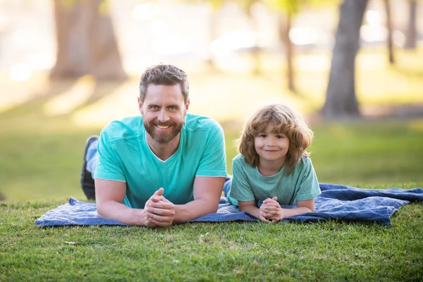 Ojciec i syn leżący na trawie w letnim parku na świeżym powietrzu. Pojęcie przyjaznej rodziny. Dzień ojców. — Zdjęcie stockowe