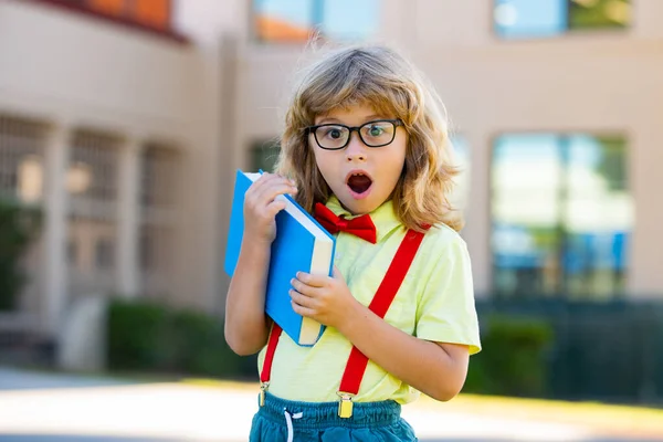 Glimlachend studentje met schoolrugzak en een oefenboek. Portret van een gelukkige leerling buiten de basisschool. Close-up gezicht van glimlachende Spaanse schooljongen kijken naar camera. — Stockfoto