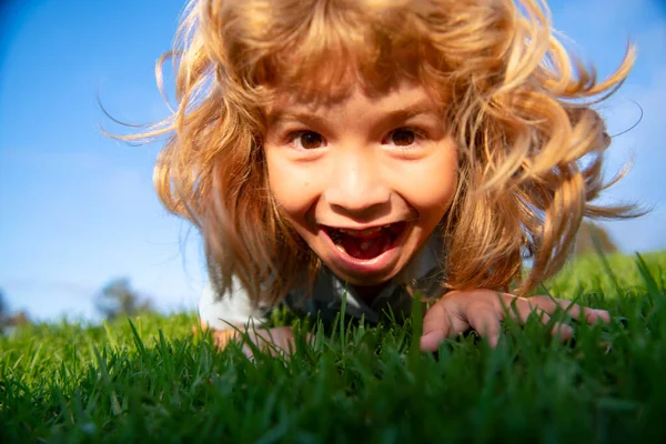 Ragazzo rosso divertente che gioca sull'erba verde nel parco, infanzia felice. Stile di vita attivo dei bambini all'aperto. Divertente ragazzo eccitato faccia in primo piano. Bambino con un viso carino espressione. — Foto Stock