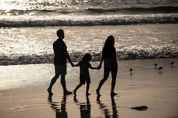 Silhouette of family walking on beach. Parents and kid walking on golden sand, mom and dad holding girls hands. Full length. Family outdoor activities concept