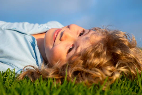 Porträtt av en leende liten pojke som ligger på grönt gräs och drömmer. Söta barn njuter av naturen utomhus. Friska bekymmerslös unge leker ute i sommarparken på en gräsmatta. — Stockfoto