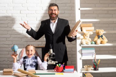 Okul dersinde eğlenceli, mutlu bir öğrenci kızla heyecanlı bir öğretmen. Mutlu komik okul çocukları. Okul üniformalı neşeli küçük kız sınıfta eğleniyor. Eğlenceli çocuk eğitimi.