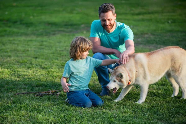 Padre e hijo jugando con el perro en el jardín. Papá y el niño con mascota divertirse al aire libre. —  Fotos de Stock