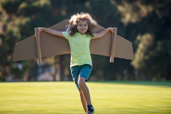 Barn flyger. Lustig pojke pilot flyger med leksakskartong flygplan vingar i parken, kopiera utrymme. Starta frihet koncept, bekymmersfri unge. — Stockfoto