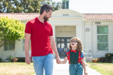 Baba oğluna okula kadar eşlik ediyor. Sırt çantalı ilkokul öğrencisinin ebeveyni ve öğrencisi..