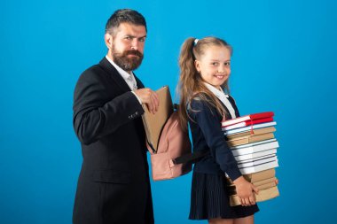 Öğretmen okul çocuğu için okul malzemeleriyle sırt çantası hazırlıyor. Elinde kitap yığını olan küçük bir kız. Çalışması zor..