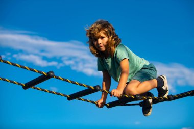 Çocuk ağa tırmanıyor. Sevimli çocuk oyun parkında merdivenleri tırmanıyor. Çocuk mavi gökyüzüne karşı merdiveni tırmanır..