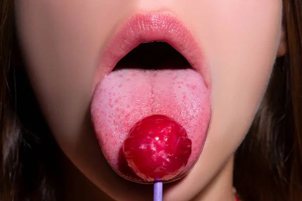 Lollipop i kvinnans mun, rött läppstift. Kvinnan slickar en röd skinande klubba. Närbild. Sexig kvinna med klubba i sexig mun. — Stockfoto