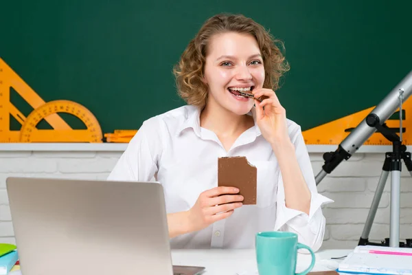 Vrouwelijke leraar eet chocolade in de klas op het schoolbord. College meisje in de klas. — Stockfoto