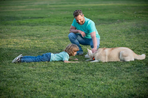 Pai e filho brincando com o cachorro no parque. Infância e paternidade conceito crianças. Pai e filho felizes brincando juntos ao ar livre. Pet amor. — Fotografia de Stock