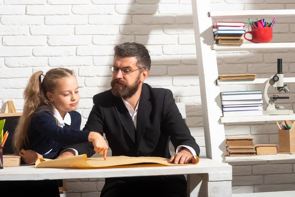 Elementare lustige Schülerin Mädchen mit ernsthaften Lehrer im Klassenzimmer. Väter und Töchter lernen. Hausaufgaben mit Papa machen. — Stockfoto