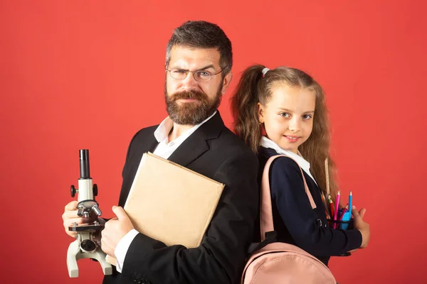 Aluno elementar com professor em estúdio vermelho, isolado. Retrato de menina da escola engraçada e tutor com material escolar. Professora feliz e estudante menina no vermelho. — Fotografia de Stock