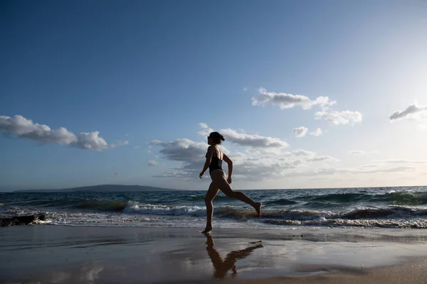 Uma mulher corre na praia. Menina desportiva correndo à beira-mar na praia tropical durante as férias. Fitness e estilo de vida saudável nas férias de verão. — Fotografia de Stock